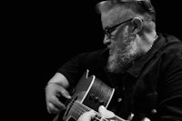 a black and white photo of a bearded man playing an acoustic guitar